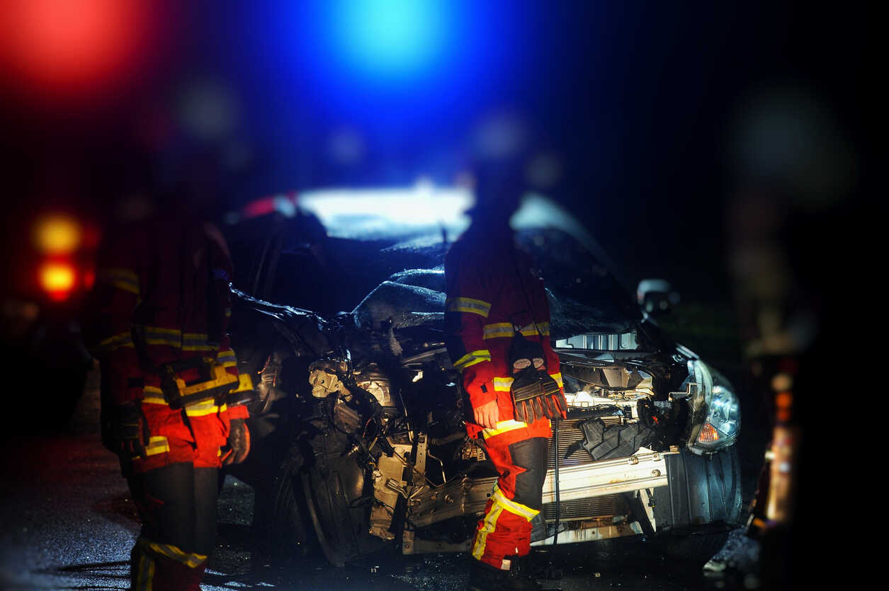 Emergency responders and flashing police lights at the scene of a severe car accident at night, indicating a potential wrongful death case.