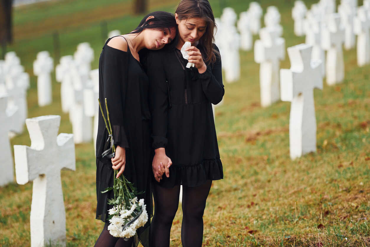 Two women in black stand grieving at a cemetery with white crosses, symbolizing the loss that can lead to a wrongful death claim in Georgia.